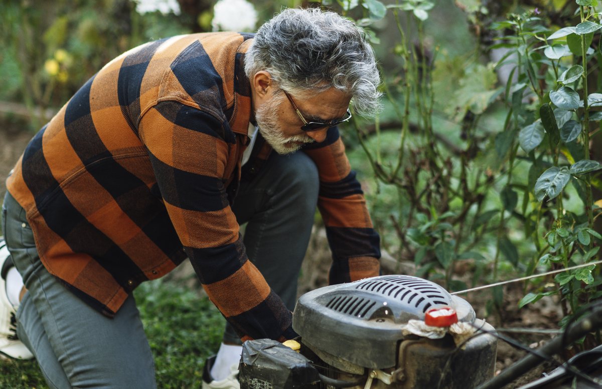 Een man herstelt de motor van een grasmaaier in een tuin