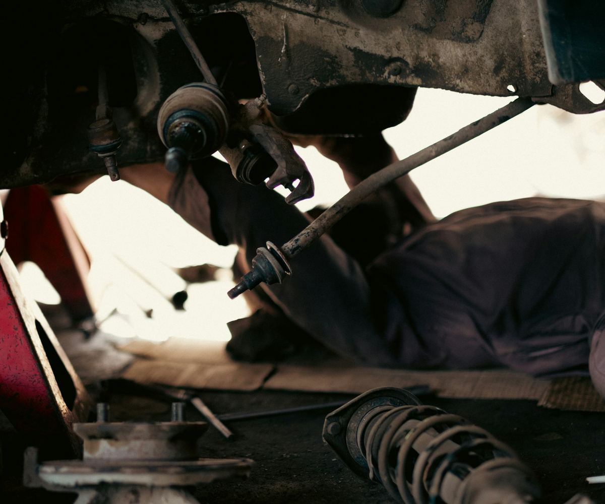 Iemand ligt onder een opgekrikte wagen, met een schokdemper en een wielnaaf op de grond